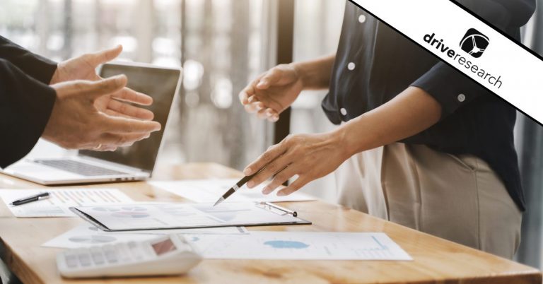 two people meeting at a desk with lots of reports for a market research kickoff meeting