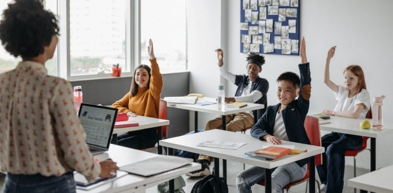 Kids raising hands in classroom with teacher