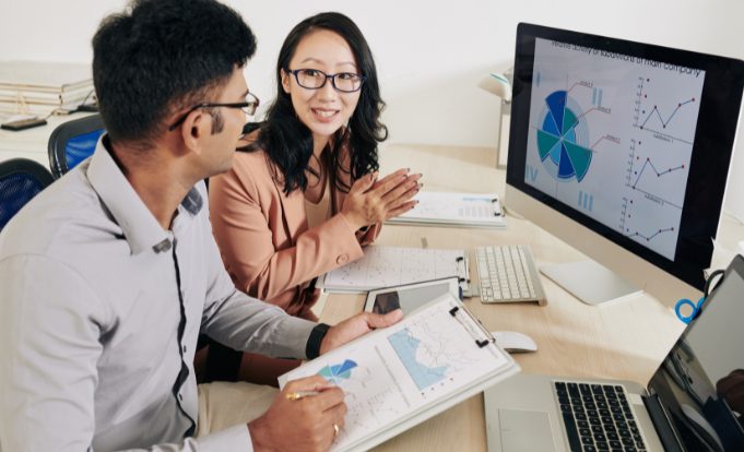 Man and woman employees at desk reviewing predictive analytics on a computer