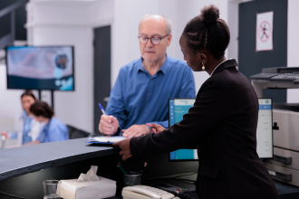 Reception worker standing at hospital counter with mystery shopping patient