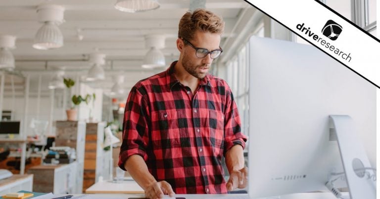 Male in plaid shirt working at a desk with a laptop