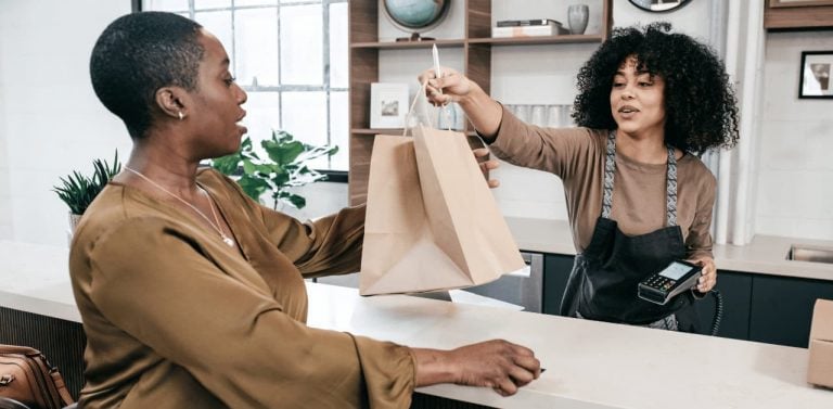 Female retail worker handing female customer a bag