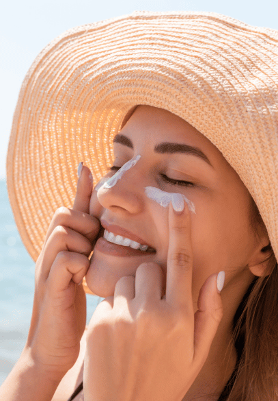 Smiling Woman in Hat Is Applying Sunscreen on Her Face