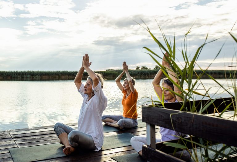 Group of senior woman doing yoga exercises by the lake