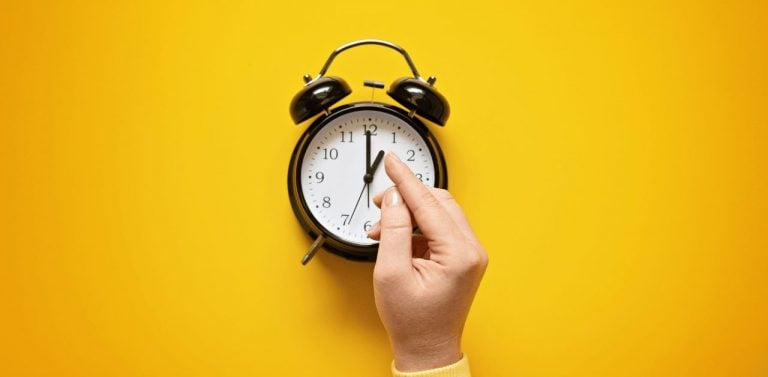 Daylight saving day. Fall Back. Black Alarm clock and female hands on yellow background. Daylight saving time end