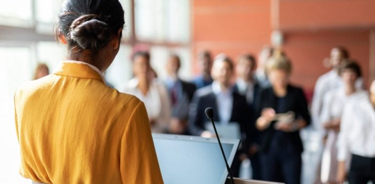 Woman speak at podium to crowd